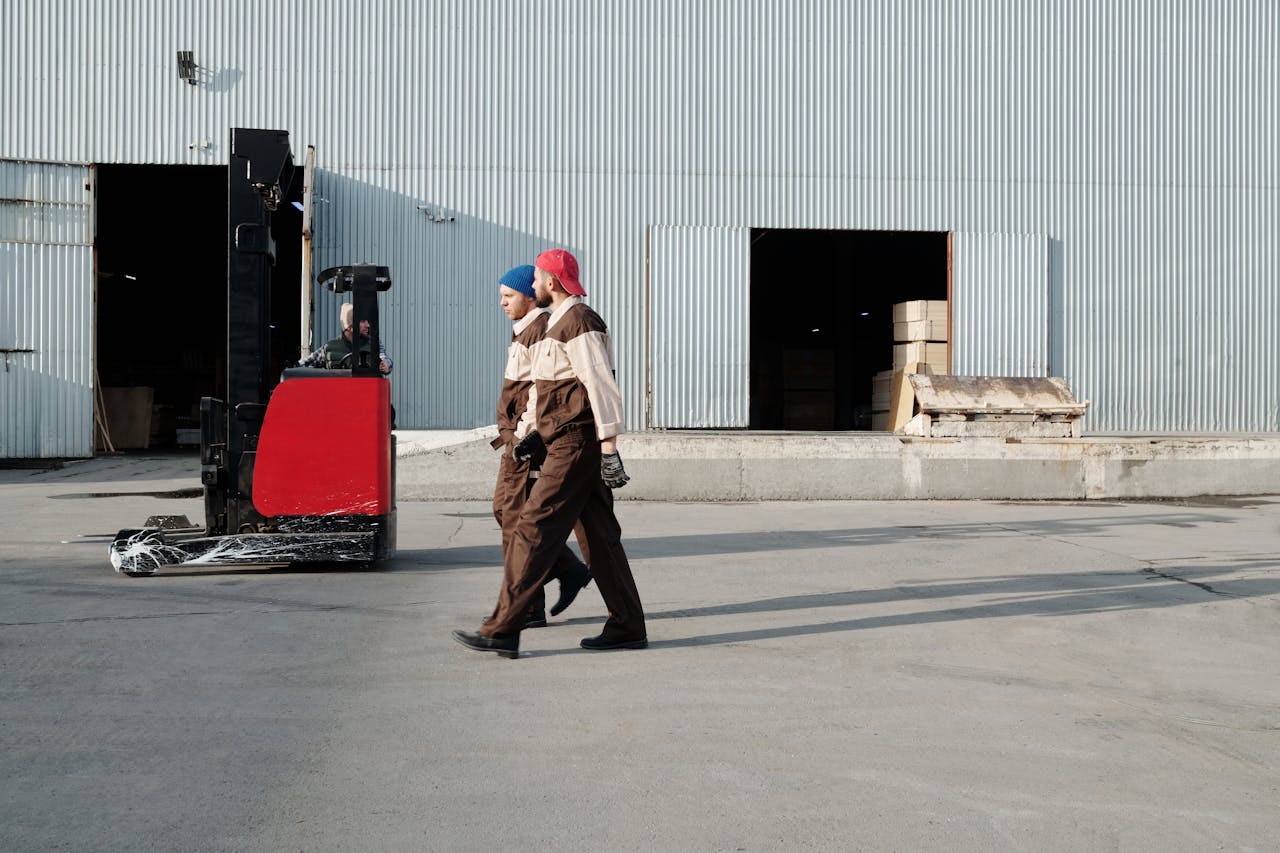 our-services-3 Two workers in uniforms walking outdoors near a forklift at a warehouse.