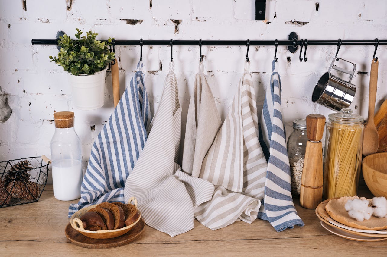 gallery-4 A cozy kitchen scene featuring striped towels, jars of pasta, milk bottle, and rustic decor on a wooden table.
