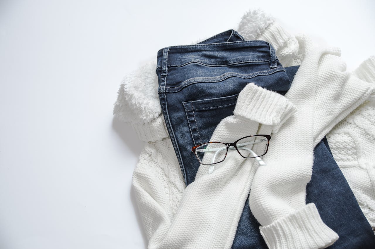 services-02 Stylish flat lay featuring denim jeans, white sweater, and eyeglasses on a bright background.